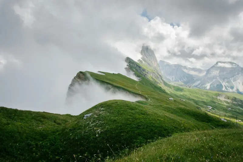 encostas verdes e picos rochosos de seceda entre nuvens, nas dolomitas italianas.