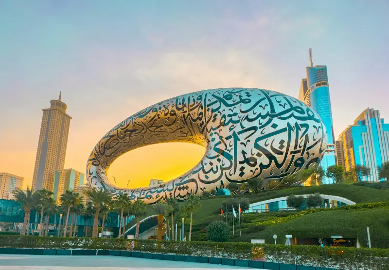 museu do futuro em dubai, com fachada curva de caligrafia árabe, jardins e torres ao fundo sob luz dourada.