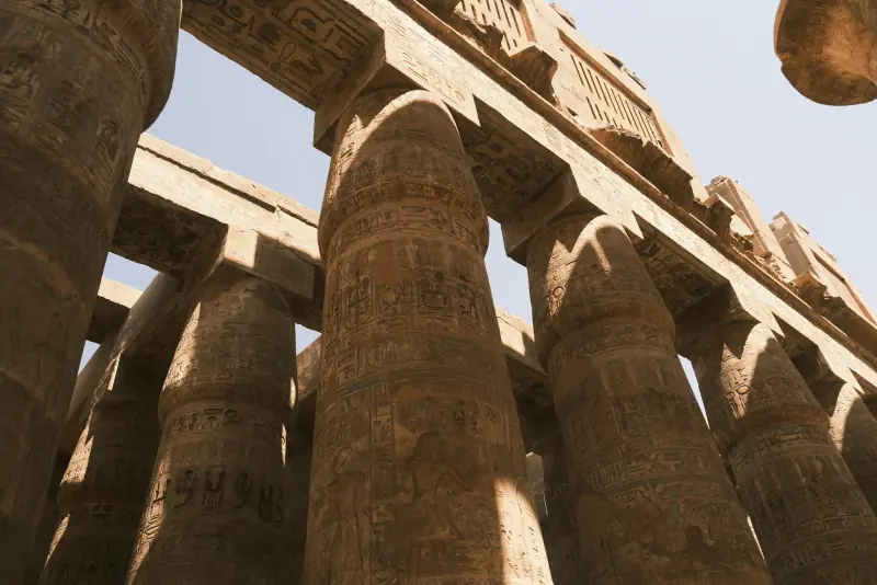 colunas monumentais cobertas de hieróglifos no complexo de karnak, em luxor, vistas de baixo sob a luz do dia.