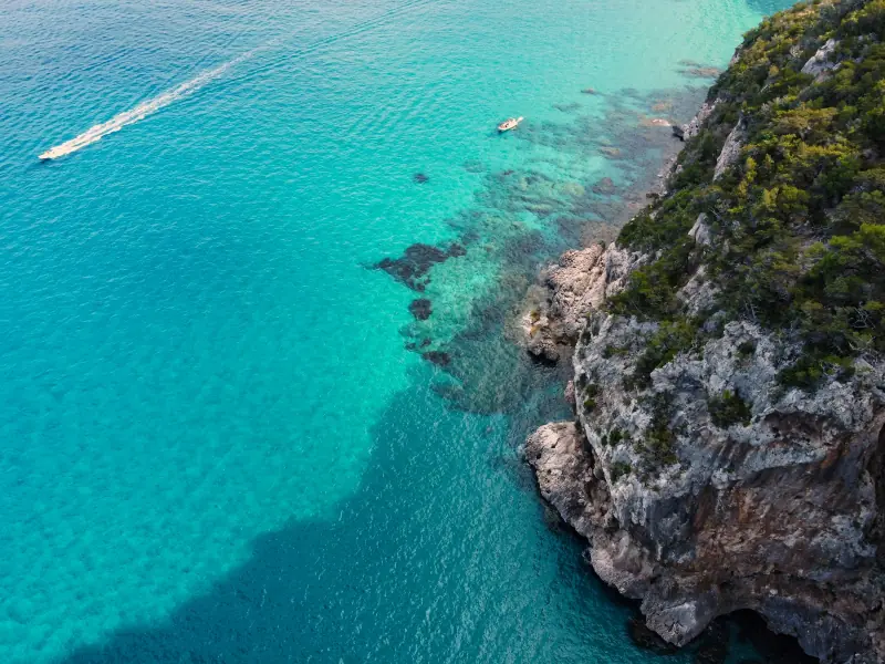 vista aérea de barcos no mar turquesa junto à costa rochosa de cala gonone, na sardenha.