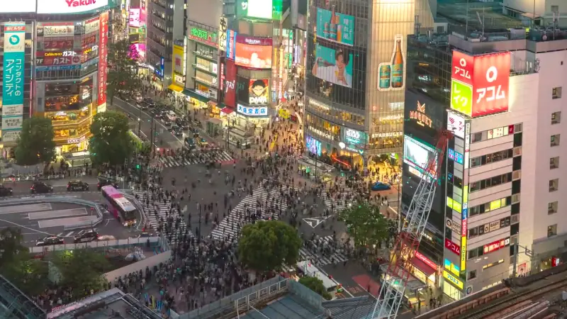 vista do alto do cruzamento de shibuya à noite, com a multidão atravessando entre prédios iluminados, em tóquio.