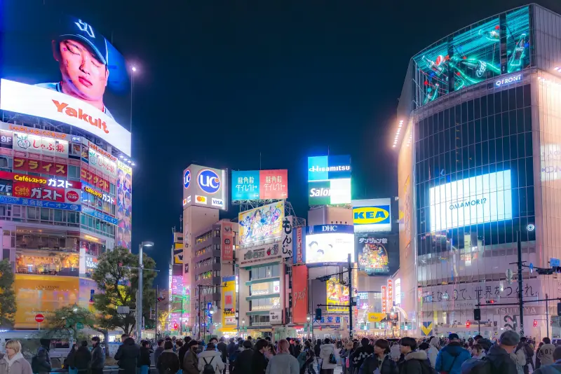 multidão diante dos painéis luminosos de shibuya à noite, em tóquio.